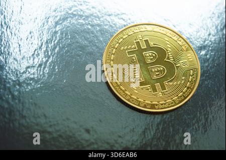 Golden Bitcoin coin placed on textured silver surface representing digital currency and investment Stock Photo