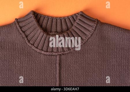 A close view of a knitted brown sweater with a ribbed collar placed on an orange background, showing the yarn texture and warm handmade autumn clothin Stock Photo