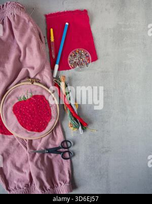 Children’s corduroy trousers with a strawberry patch placed beside sewing tools including scissors, pins and embroidery thread, shown with clear copy Stock Photo