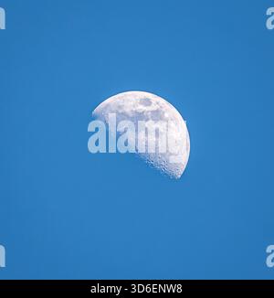 A vibrant image capturing a beautiful half-moon in a clear blue sky during daylight hours, showcasing the detailed lunar surface under the brilliance Stock Photo