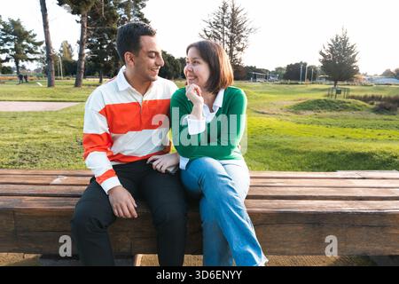 A young Latin couple shares a cozy moment on a park bench, surrounded by a serene outdoor landscape, hinting at strong emotional bonds and contentment Stock Photo