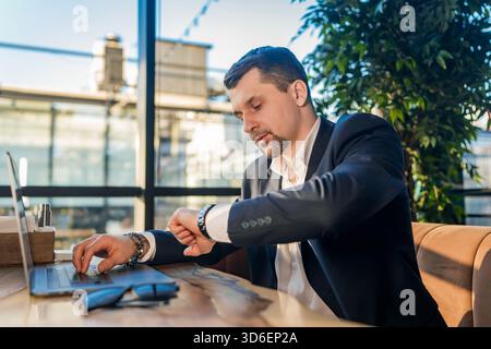 A businessman in a suit works on his laptop in a stylish cafe filled with natural light Stock Photo