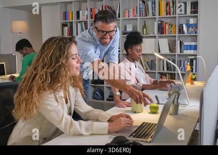 Male and female coworkers discussing project while working in office with diverse colleagues Stock Photo