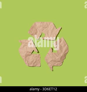 Crumpled brown paper forms the recycling symbol, conceptually illustrating waste reduction and environmental awareness on a vibrant green backdrop. Stock Photo