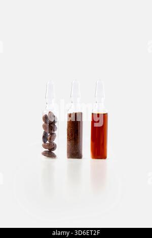 Three small glass vials against a white background, filled with different states of coffee; the first contains whole coffee beans, the second ground c Stock Photo