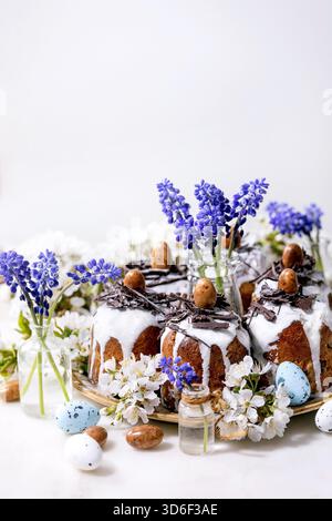Homemade traditionla Easter kulich cake with chocolate nests and eggs, blossoming cherry branches and muscari flowers over white marble background. Traditional ortodox Easter Russian Ukrainian bake Stock Photo