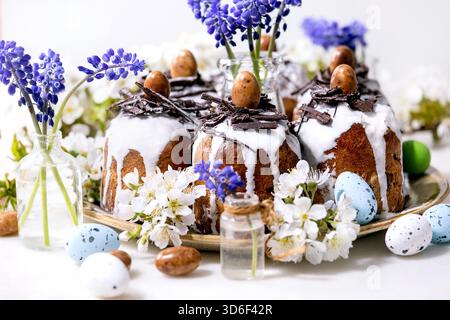 Homemade traditionla Easter kulich cake with chocolate nests and eggs, blossoming cherry branches and muscari flowers over white marble background. Traditional ortodox Easter Russian Ukrainian bake Stock Photo