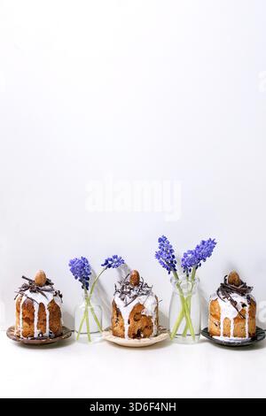 Homemade traditionla small Easter kulich cakes with chocolate nests and eggs on plates in row decorated with muscari flowers over white marble table. Traditional ortodox Easter Russian Ukrainian bake Stock Photo