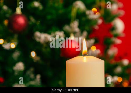 Close-up Christmas candle flame with bright festive tree lights and ornaments softly blurred behind for warm seasonal themes Stock Photo
