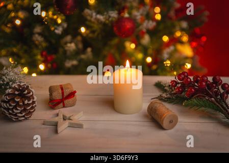 Candle burning on a decorated wooden table with pine branches, berries, gifts and warm holiday lights creating a cozy Christmas mood Stock Photo