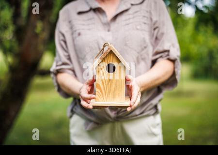 Woman holding small handmade wooden birdhouse in garden, ready to hang on tree Stock Photo
