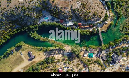 Idyllic summer vacation scene from above, highlighting the clear emerald water of a river next to houses, roads, and recreational facilities Stock Photo