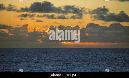 A photo of the darkening atmosphere as the sun sets over the ocean horizon Stock Photo