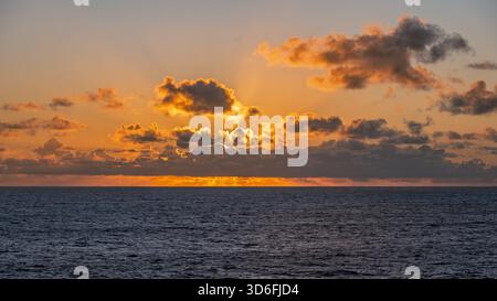 A photo of the sun setting over the horizon, casting a warm glow on the water and clouds above Stock Photo