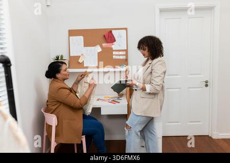 Female colleagues collaborating on design at home design studio using tablet and lace hanger Stock Photo