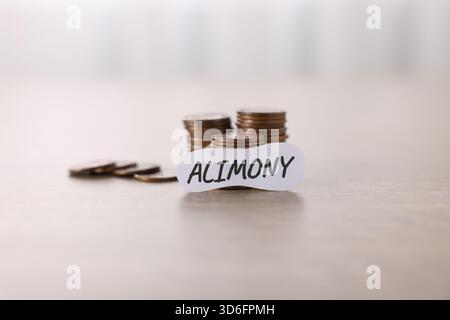 Paper note with word Alimony and stack of coins on wooden table, closeup Stock Photo