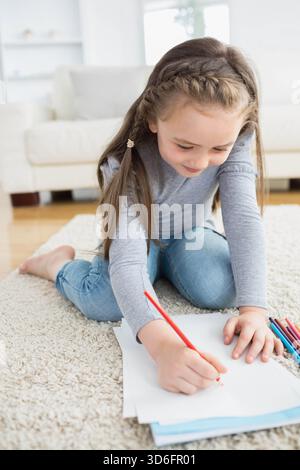 Child sitting on light shag rug in living room drawing with red colored pencil and papers. Kid, art, craft, home, bright, calm, cozy Stock Photo