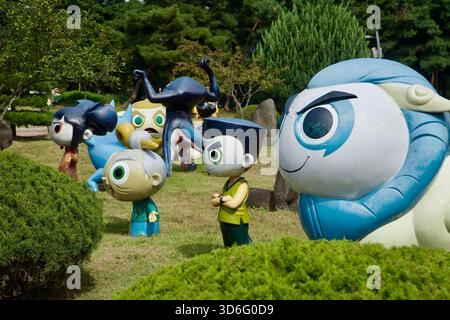 Colorful character figures stand among trimmed shrubs on the museum lawn, including a blue ram-like mascot and a black creature mid-pose, part of the Stock Photo