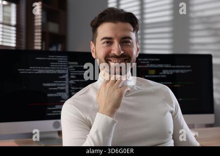 Portrait of smiling programmer in front of computer with dual monitors at workplace Stock Photo