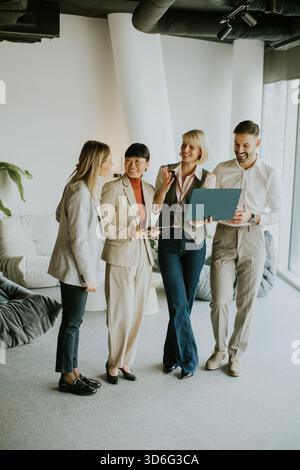 Four professionals gather in a stylish office space, sharing ideas and insights while standing near a large window. Sunlight fills the room, creating Stock Photo