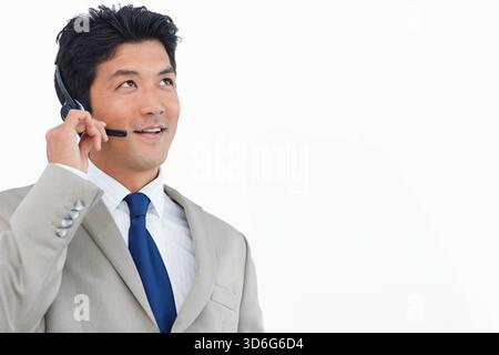 Asian man wearing light gray suit blue tie adjusting headset while smiling in studio, copy space. Headphones, portrait, corporate, professional, busin Stock Photo