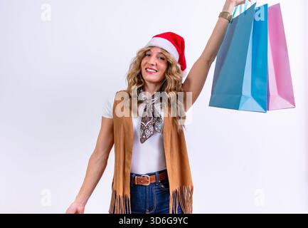 Woman smiling, holding up multiple shopping bags, wearing a santa hat Stock Photo