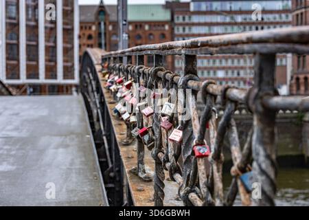 Love locks attached to the rusty railing of a historic bridge in Hamburg’s Speicherstadt, with old brick buildings and canal views in the back Stock Photo
