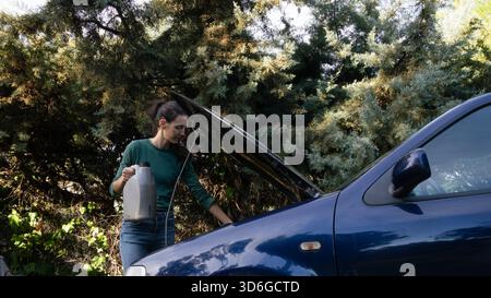 Woman filling car engine oil during routine maintenance under open hood Stock Photo