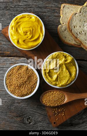Mustard still life with two different mustards in ramekins, Rye bread and mustard seeds on a cutting board. Stock Photo