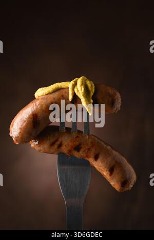Two grilled sausages on fork with mustard Stock Photo