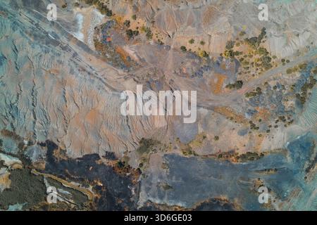 Vertical drone shot illustrating severe land degradation. Abstract pattern showing layered erosion of a spoil heap and a dramatic contrast with black, scorched earth from chemical runoff. Stock Photo