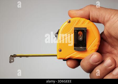 Hand holding a yellow retractable tape measure, with the metal blade slightly extended. Stock Photo