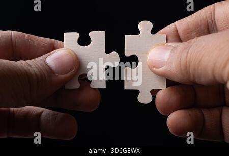 Macro shot of two hands connecting two wooden jigsaw puzzle pieces in a moment of solution. Stock Photo
