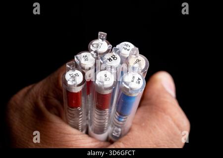 Close-up of a hand holding multiple colored pen refills against a black background. Stock Photo