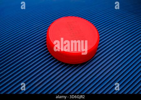 Vibrant Red Round Plastic Cap on Deeply Textured Diagonal Blue Ribbed Surface Stock Photo