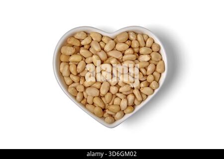peeled pine nuts in a white heart-shaped bowl isolated on white background. Stock Photo