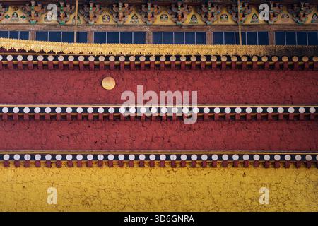 View of vibrant layers of red, yellow, and gold adorn a textured wall under a dark blue window, showcasing intricate designs, Diqing Tibetan Autonomou Stock Photo