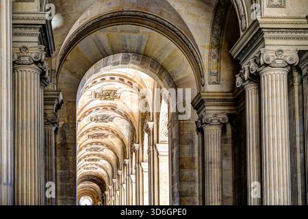 Black and white view of the vaulted stone colonnade at the Louvre Museum in Paris, showing repeating arches and classical detail. Stock Photo
