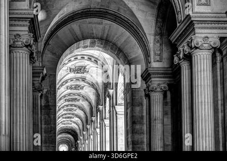 Black and white view of the vaulted stone colonnade at the Louvre Museum in Paris, showing repeating arches and classical detail. Stock Photo