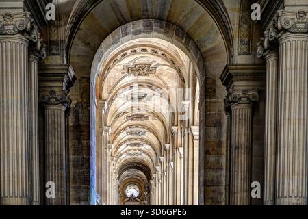 Black and white view of the vaulted stone colonnade at the Louvre Museum in Paris, showing repeating arches and classical detail. Stock Photo
