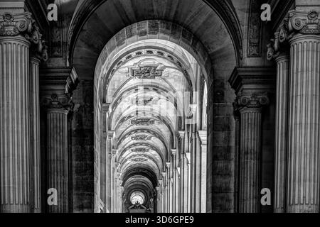 Black and white view of the vaulted stone colonnade at the Louvre Museum in Paris, showing repeating arches and classical detail. Stock Photo