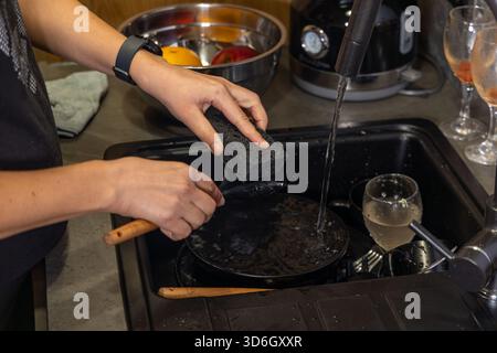 Person washing kitchen spatula under running water. Close-up of hands cleaning a kitchen spatula with a sponge under running tap water in a domestic Stock Photo