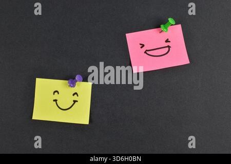 Yellow and pink sticky notes with smiley faces on black background, expressing emotion and contrast through minimal design and color. Stock Photo