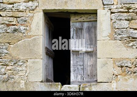 Natural stone wall with window and half-open unpainted and wheathered wooden shutters or blinds in Cornac Lot Occitanie in Southern France Stock Photo