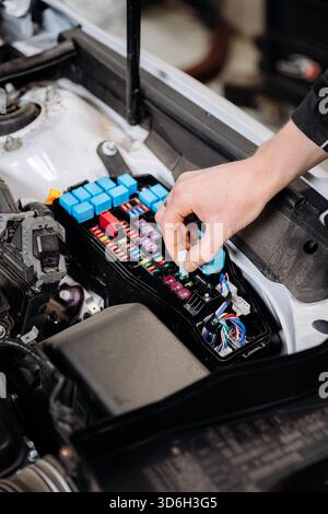 Mechanic replacing car fuse in engine bay fuse box, auto service maintenance close up Stock Photo