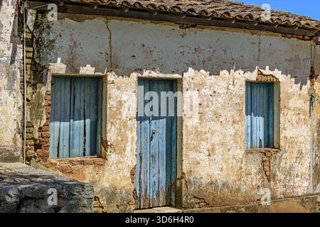 An old, abandoned house, ravaged by time, with its blue windows and crumbling plaster on the walls Stock Photo