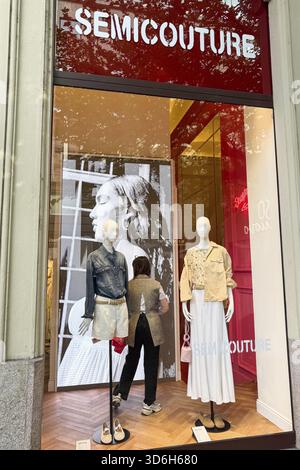 Milan, Italy - April, 12, 2025: SEMICOUTURE storefront in Milan. Two mannequins with denim and neutral outfits in front of video screen and red wall Stock Photo
