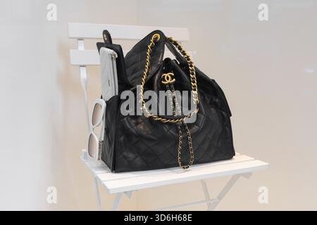 Milan, Italy - April, 12, 2025: Chanel quilted leather handbag with gold chain logo detail on white chair in luxury boutique display Stock Photo