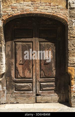 Close up of an ancient wooden door with iron details, set within a rustic stone arch, embodying old world charm Stock Photo
