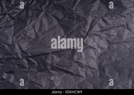 Dark wrinkled creased black paper poster texture. Blank creased crumpled grainy paper textured surface. Smudged grungy cardboard with fiber. Close up. Stock Photo